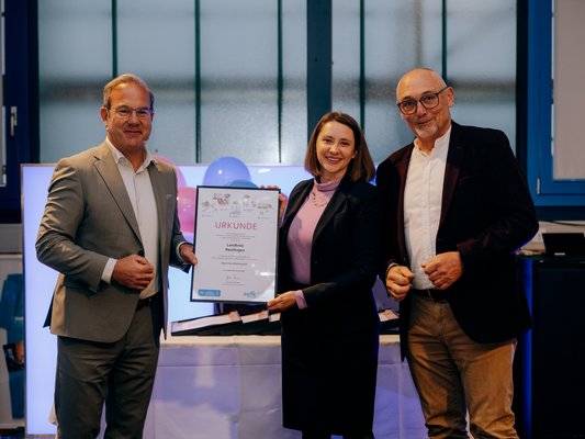 Die Erste Landesbeamtin des LK RT, Greta Schirmer-Förster (m.), nimmt die Ehrung im Namen der Kreisverwaltung von Günter Riemer (r.), Vorstand der AGFK BW, und Staatssekretär Raimund Haser (l.) entgegen. (Fotoquelle: AGFK-BW/Ilkay Karakurt)
